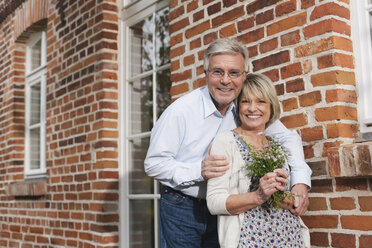 Germany, Kratzeburg, Senior couple with flower bouquet at country house, smiling, portrait - WESTF016700