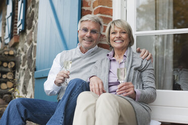 Germany, Kratzeburg, Senior couple sitting on terrace of country house with champagne flute - WESTF016703