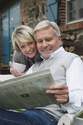 Germany, Kratzeburg, Senior couple sitting on terrace of country house and reading newspaper - WESTF016704