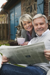 Deutschland, Kratzeburg, Älteres Paar auf der Terrasse eines Landhauses mit Zeitung - WESTF016705