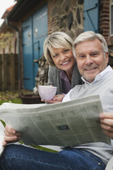 Germany, Kratzeburg, Senior couple sitting on terrace of country house with newspaper - WESTF016705