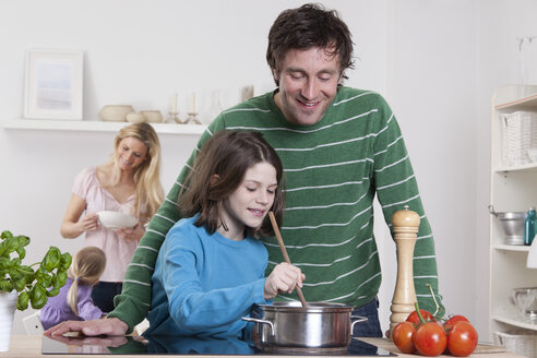 Deutschland, Bayern, München, Sohn kocht mit Vater, Mutter und Tochter im Hintergrund - RBF000640