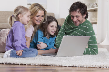 Deutschland, Bayern, München, Familie liegt auf Teppich und benutzt Laptop, lächelnd - RBF000647