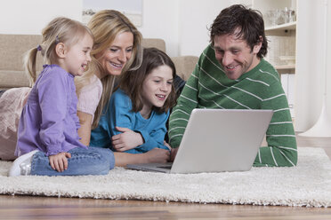 Germany, Bavaria, Munich, Family lying on carpet and using laptop, smiling - RBF000647