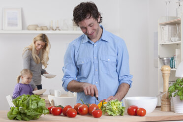 Deutschland, Bayern, München, Vater bereitet Salat mit Mutter und Tochter im Hintergrund zu - RBF000628