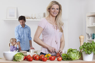 Deutschland, Bayern, München, Mutter bereitet Salat mit Vater und Tochter im Hintergrund zu - RBF000632