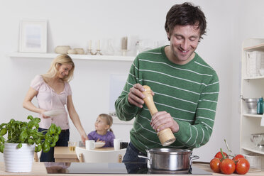 Deutschland, Bayern, München, Vater kocht mit Mutter und Tochter im Hintergrund - RBF000636