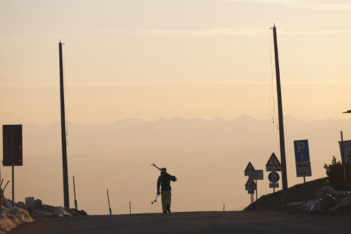 Italien, Trentino-Südtirol, Südtirol, Bozen, Seiser Alm, Mittlerer erwachsener Mann mit Skiern auf der Straße am Morgen - MIRF000155