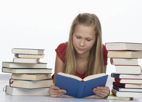 Mädchen liest ein Buch neben einem Stapel von Büchern vor weißem Hintergrund, lizenzfreies Stockfoto