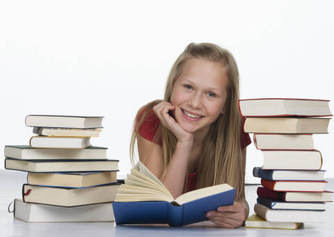 Mädchen hält ein Buch neben einem Stapel von Büchern vor weißem Hintergrund, lächelnd, Porträt, lizenzfreies Stockfoto