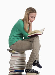 Mädchen sitzt und liest auf einem Stapel von Büchern vor weißem Hintergrund - WWF001905