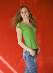 Europe, Teenage girl turning back with red wall in background, smiling, portrait - WWF001914