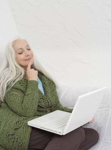 Deutschland, Düsseldorf, Frau mit Laptop auf Sofa, Augen geschlossen, lizenzfreies Stockfoto