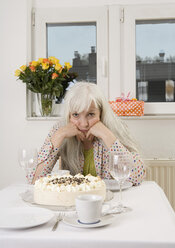 Deutschland, Düsseldorf, Frau am Esstisch sitzend mit Kuchen, Blumenvase und Geschenk, Porträt - UKF000211