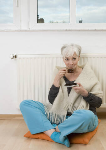 Deutschland, Düsseldorf, Frau trinkt Tee bei Heizung zu Hause, lächelnd, Porträt, lizenzfreies Stockfoto