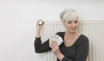 Deutschland, Düsseldorf, Frau hält Geldscheine in der Hand und stellt Heizung ein, lächelnd, Porträt - UKF000220