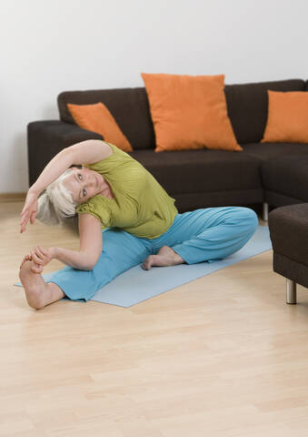 Germany, Duesseldorf, Woman doing yoga near sofa at home stock photo