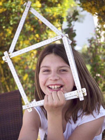 Nahaufnahme eines Mädchens, das ein Haus aus Zollstöcken hält, lächelnd, Porträt, lizenzfreies Stockfoto