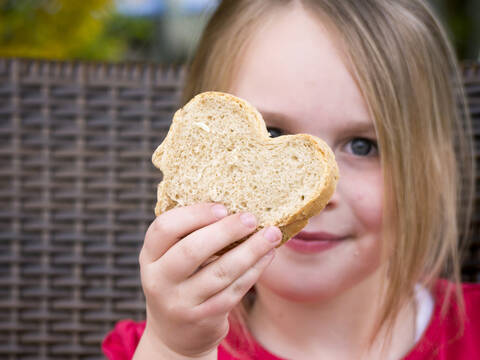 Deutschland, Bayern, Nahaufnahme eines Mädchens, das eine Brotscheibe hält, lächelnd, Porträt, lizenzfreies Stockfoto