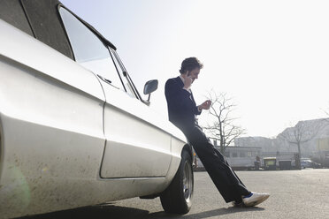 Germany, Hamburg, Mid adult man leaning on classic car and talking on mobile phone - DBF000086