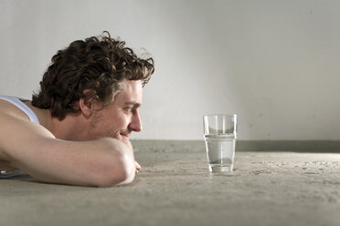 Mid adult man lying on floor and staring at glass of water - DBF000094