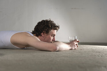 Mid adult man lying on floor and staring at glass of water - DBF000095