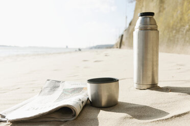 Germany, Hamburg, Close up of newspaper and thermos flask at beach near Elbe riverside - DBF000120