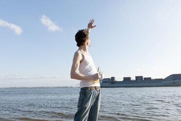 Germany, Hamburg, Man with beer bottle near Elbe riverside and container ship in background - DBF000132