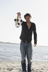 Germany, Hamburg, Man holding torn football near Elbe riverside - DBF000134