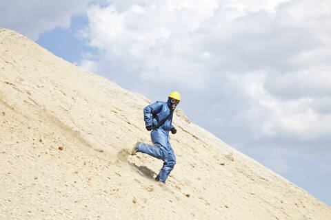 Deutschland, Bayern, Mann in Arbeitsschutzkleidung läuft am Hang einer Sanddüne, lizenzfreies Stockfoto