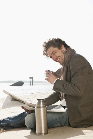 Germany, Hamburg, Mid adult man drinking and reading newspaper near Elbe river, smiling, portrait stock photo