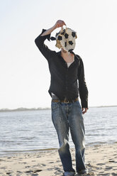 Deutschland, Hamburg, Mittlerer erwachsener Mann, der sein Gesicht mit einem zerrissenen Fußball bedeckt, in der Nähe der Elbe - DBF000074
