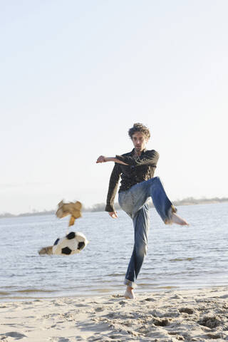 Germany, Hamburg, Mid adult man kicking torn football near Elbe river stock photo