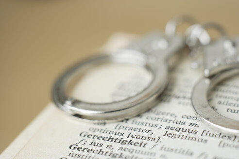 Handcuffs on dictionary against coloured background, close up - TCF001508