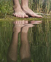 Austria, Vienna, Reflection of man's feet on lakeshore, close up - MBEF000108