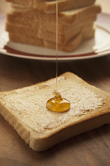 Germany, North Rhine-Westphalia, Düsseldorf, Close up of honey falling on toast - KJF000098