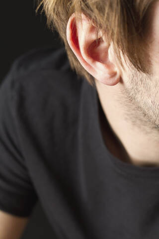 Ohr eines jungen Mannes mit Bartstoppeln vor schwarzem Hintergrund, Nahaufnahme, lizenzfreies Stockfoto
