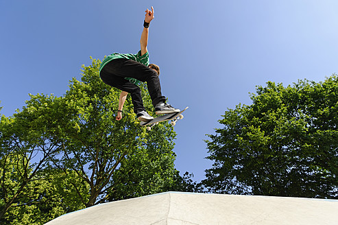 Germany, Duesseldorf, Young man performing tricks with skateboard in skatepark - KJF000106