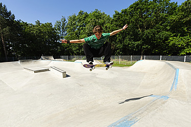 Germany, Duesseldorf, Young man performing tricks with skateboard in skatepark - KJF000105