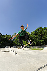 Germany, Duesseldorf, Young man performing tricks with skateboard in skatepark - KJF000104