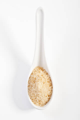 Brauner Zucker in Porzellanlöffel auf weißem Hintergrund, lizenzfreies Stockfoto