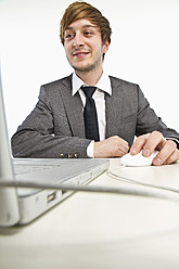 Young businessman working on laptop against white background - MBEF000142