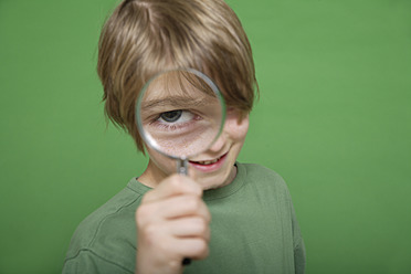 Close up of boy looking through magnifying glass against green background - TCF001563