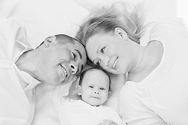Deutschland, Bayern, Vater, Mutter und Tochter auf Decke liegend, lächelnd - RNF000603