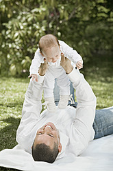 Germany, Bavaria, Father holding daughter lying on blanket in garden, smiling - RNF000604