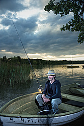 Deutschland, Bayern, Wörthsee, Mann mit Laterne beim Fischen im Boot in der Abenddämmerung - RNF000606