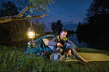 Deutschland, Bayern, Ammersee, Mann schenkt beim nächtlichen Camping am Seeufer ein Getränk ein - RNF000614