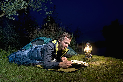 Deutschland, Bayern, Ammersee, Mann liest Buch am Seeufer beim nächtlichen Camping - RNF000615
