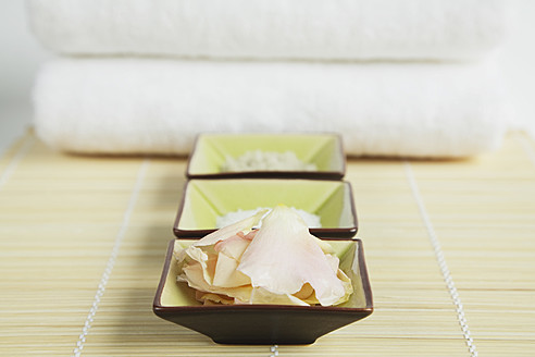 Nahaufnahme einer Schale mit Rosenblättern, grauem Badesalz und Handtuch auf einer Bambusmatte - GWF001501