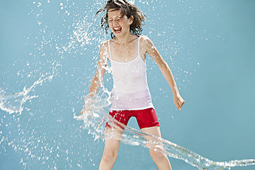 Deutschland, Mädchen springt in Wasserspritzer vor blauem Hintergrund - MAEF003421